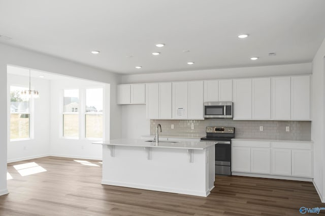 kitchen with sink, appliances with stainless steel finishes, a kitchen island with sink, backsplash, and white cabinets