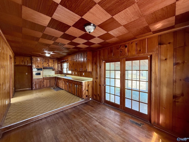 kitchen featuring wooden walls, brown cabinetry, visible vents, and oven