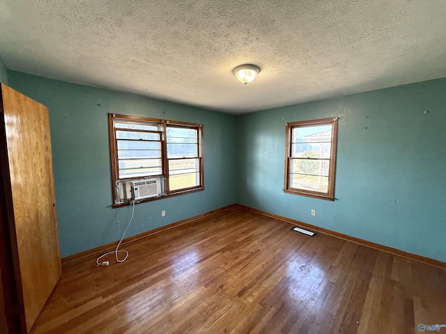 empty room with cooling unit, wood finished floors, visible vents, baseboards, and a textured ceiling