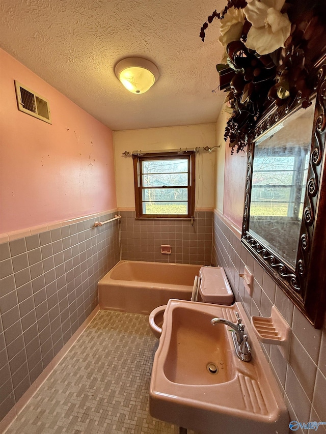 bathroom with visible vents, a sink, a textured ceiling, tile walls, and a bathtub