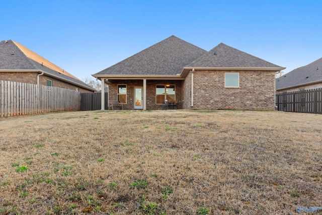 rear view of property featuring a yard, brick siding, a fenced backyard, and a shingled roof