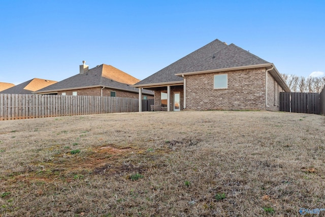 rear view of property with brick siding, a fenced backyard, a lawn, and a shingled roof