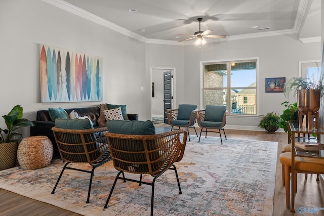 living area with a ceiling fan, wood finished floors, baseboards, and ornamental molding