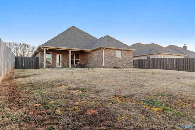 rear view of property featuring a lawn, a fenced backyard, brick siding, and a shingled roof