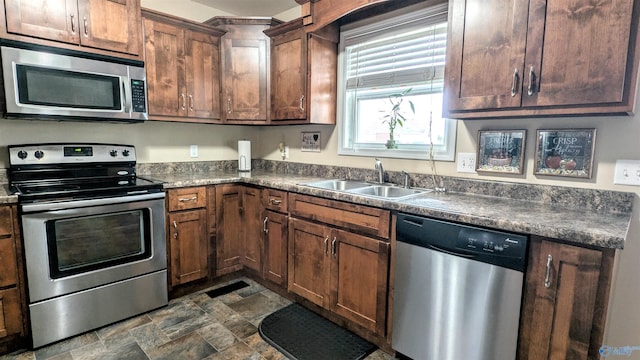 kitchen with dark countertops, stone finish floor, appliances with stainless steel finishes, and a sink