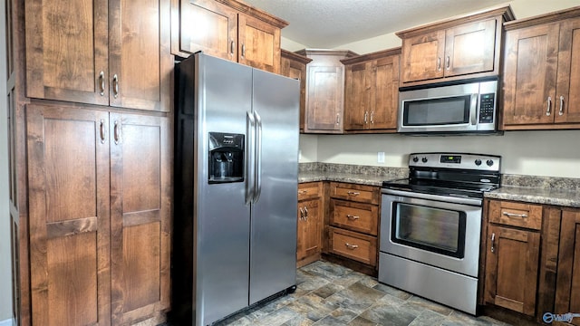 kitchen with a textured ceiling, stainless steel appliances, and stone finish flooring