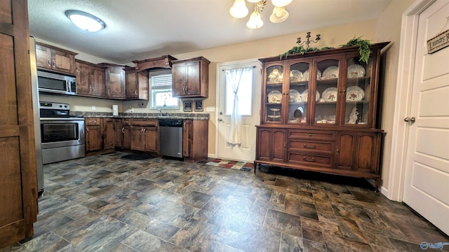 kitchen with stone finish floor, dark countertops, stainless steel appliances, dark brown cabinetry, and a chandelier