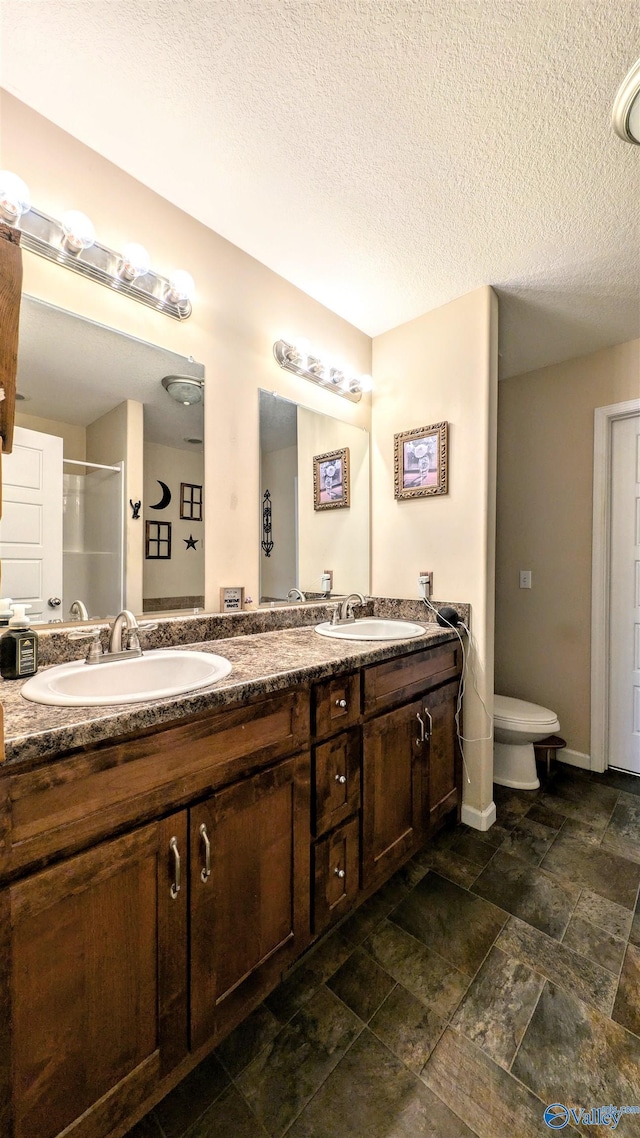 full bath with a sink, a textured ceiling, a stall shower, and double vanity