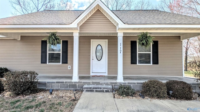 view of exterior entry with roof with shingles and covered porch