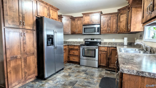 kitchen with dark countertops, stainless steel appliances, stone finish floor, a textured ceiling, and a sink