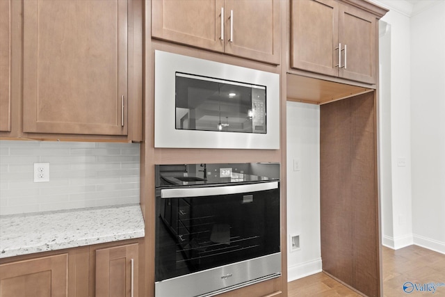 kitchen with built in microwave, light stone counters, light hardwood / wood-style flooring, wall oven, and backsplash