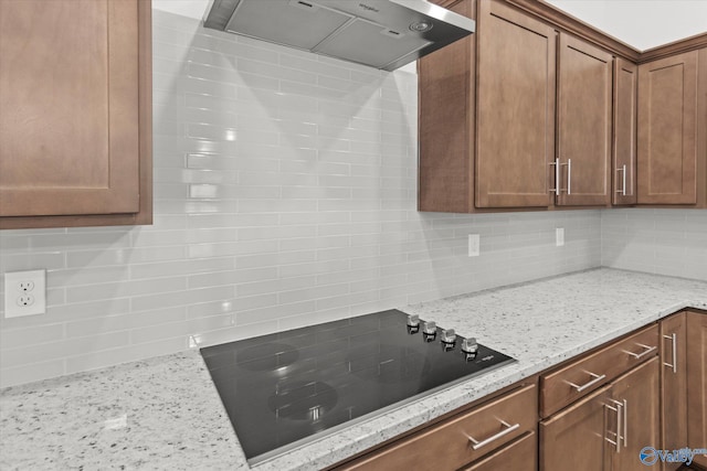 kitchen featuring light stone counters, black electric stovetop, decorative backsplash, and wall chimney range hood