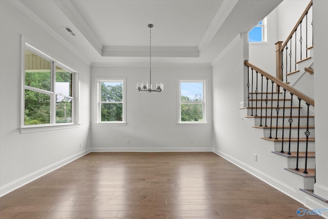 unfurnished dining area with an inviting chandelier, a tray ceiling, dark wood-type flooring, and ornamental molding