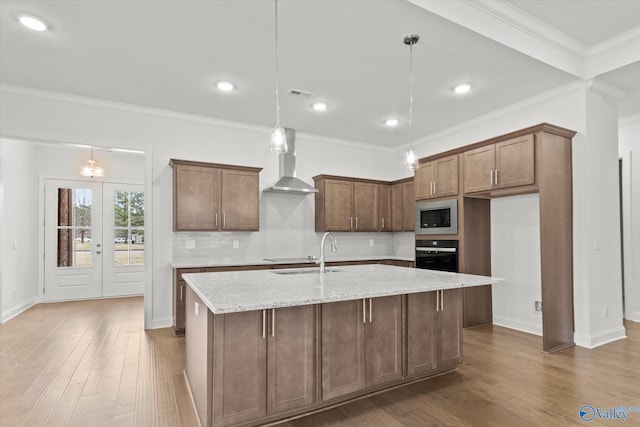 kitchen featuring black oven, hanging light fixtures, light stone counters, built in microwave, and wall chimney exhaust hood