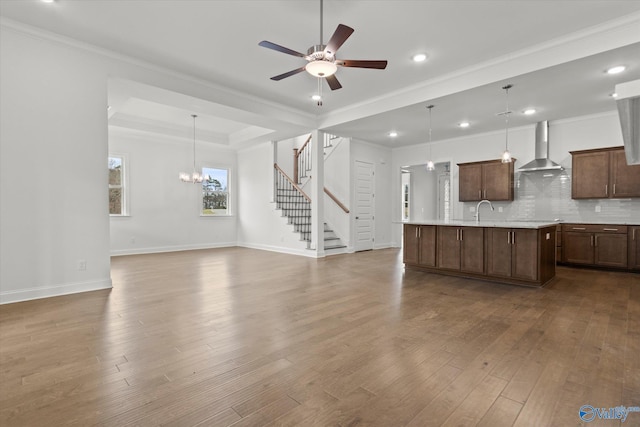 unfurnished living room with sink, crown molding, hardwood / wood-style floors, ceiling fan with notable chandelier, and a raised ceiling