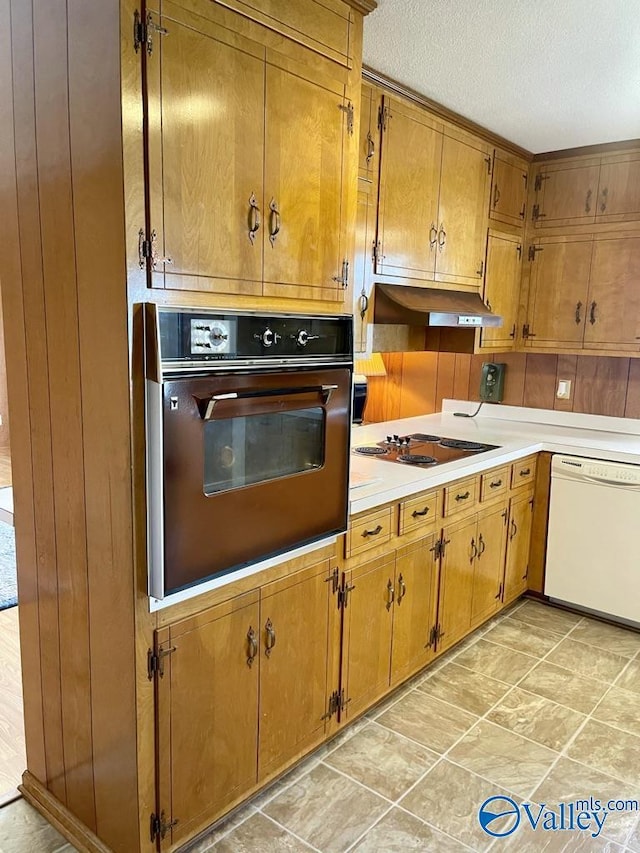 kitchen featuring light countertops, electric cooktop, wall oven, dishwasher, and under cabinet range hood