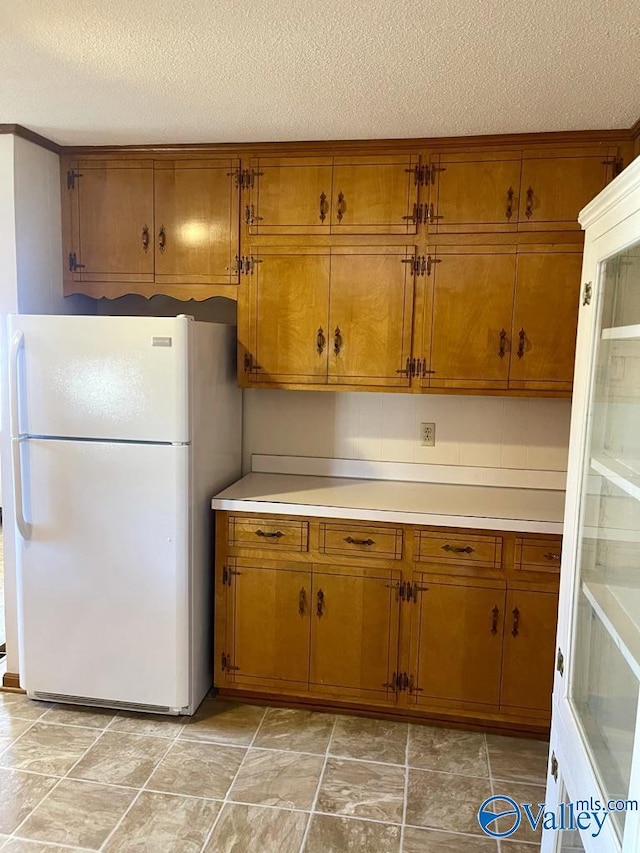 kitchen featuring a textured ceiling, light countertops, freestanding refrigerator, and brown cabinets