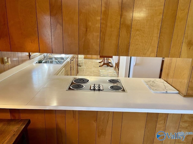 kitchen featuring stainless steel electric cooktop, brown cabinets, light countertops, and a sink