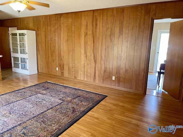 unfurnished room with ceiling fan, wood finished floors, and wooden walls