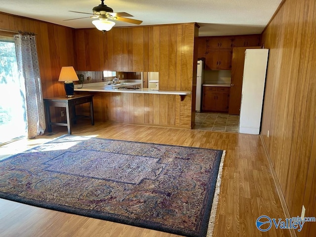 kitchen with a peninsula, light wood-style floors, wooden walls, and brown cabinets