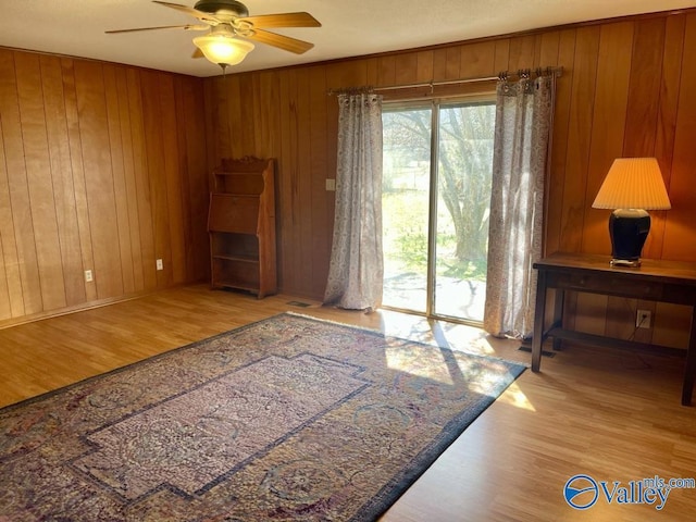 interior space featuring ceiling fan, wooden walls, and wood finished floors