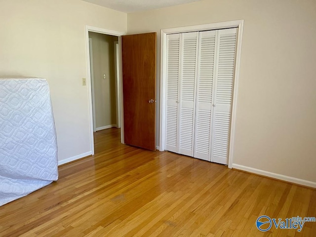 unfurnished bedroom featuring light wood-style floors, a closet, and baseboards