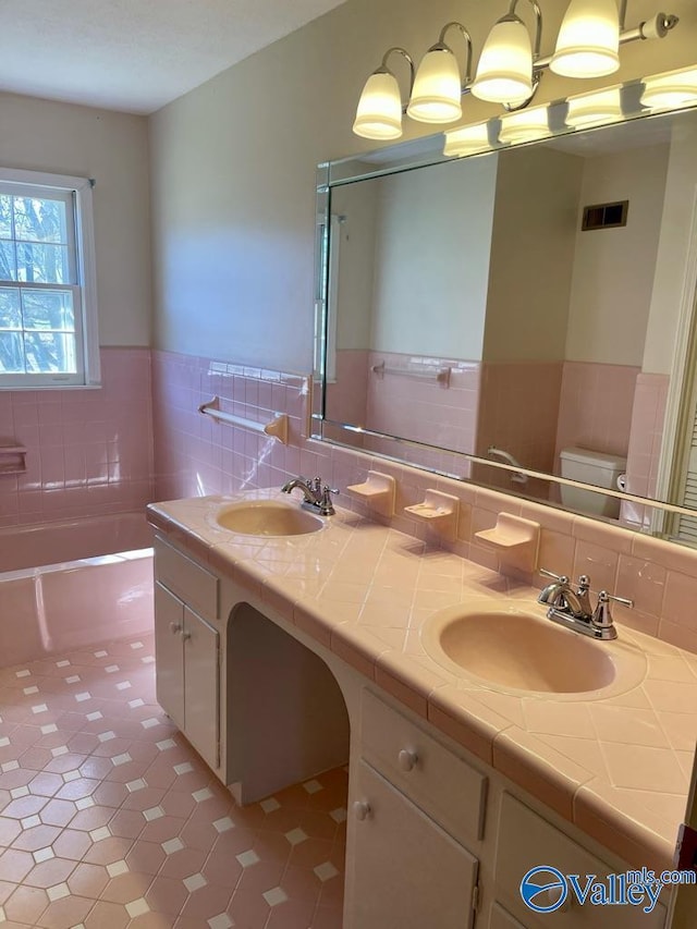 full bathroom featuring a tub to relax in, visible vents, a sink, and double vanity