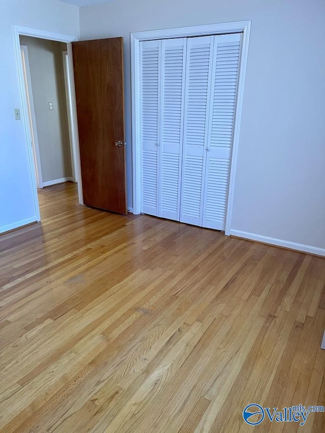 unfurnished bedroom featuring light wood-style floors, baseboards, and a closet