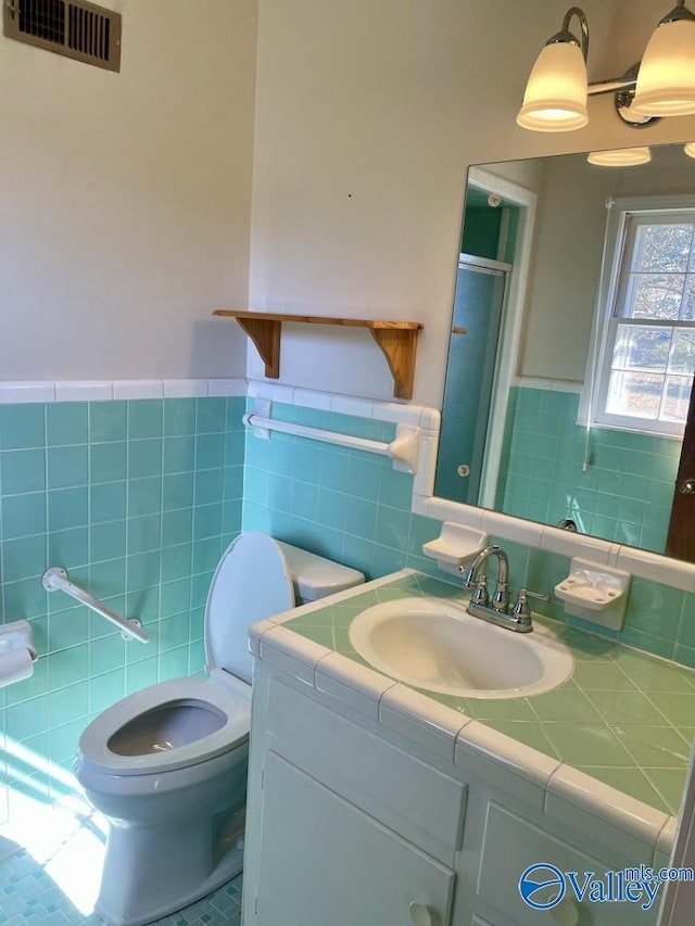 full bathroom with tile walls, visible vents, toilet, an enclosed shower, and vanity