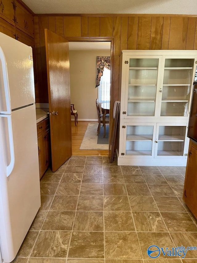 kitchen featuring wooden walls, freestanding refrigerator, and brown cabinets