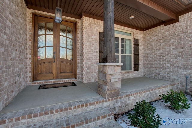 view of exterior entry with brick siding, a porch, and french doors