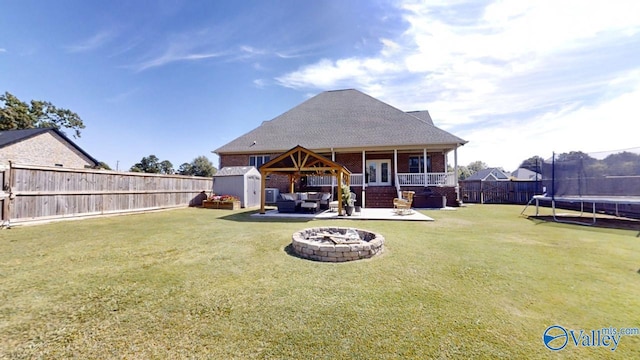 back of house featuring a patio area, a trampoline, a storage shed, a yard, and an outdoor fire pit