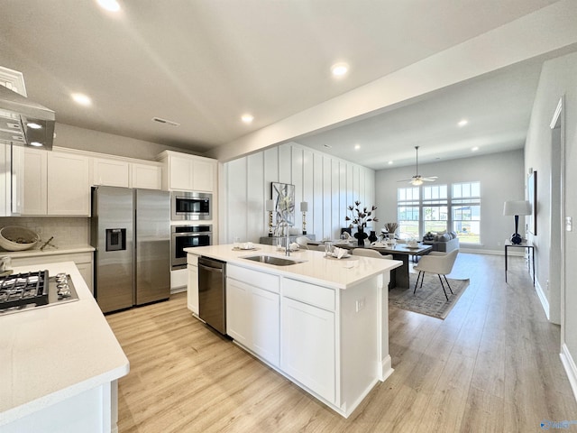 kitchen with ceiling fan, white cabinets, an island with sink, appliances with stainless steel finishes, and light hardwood / wood-style floors