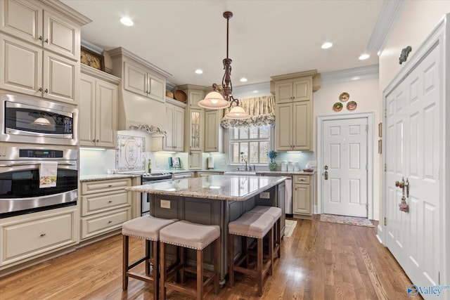 kitchen with stainless steel appliances, cream cabinets, a sink, and a kitchen breakfast bar