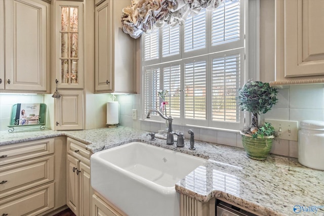 kitchen featuring glass insert cabinets, a sink, light stone countertops, cream cabinetry, and backsplash