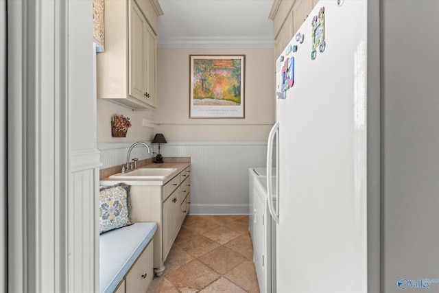 washroom featuring crown molding, cabinet space, wainscoting, a sink, and separate washer and dryer