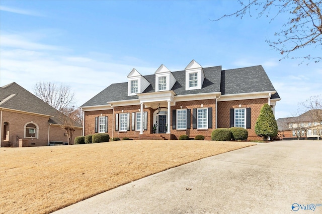 view of front of house with brick siding, a front lawn, and roof with shingles