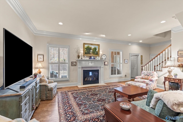 living room featuring light wood-style flooring, a fireplace with flush hearth, stairway, crown molding, and recessed lighting