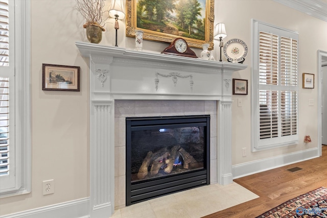 details with wood finished floors, visible vents, baseboards, ornamental molding, and a tiled fireplace