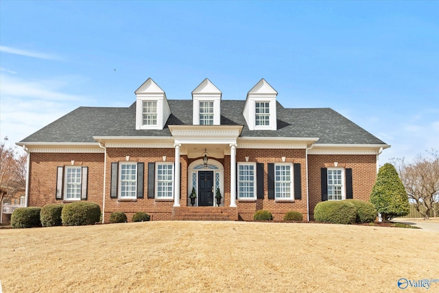 view of front of home with a shingled roof, a front yard, and brick siding