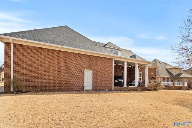 rear view of property featuring a shingled roof, a ceiling fan, and brick siding