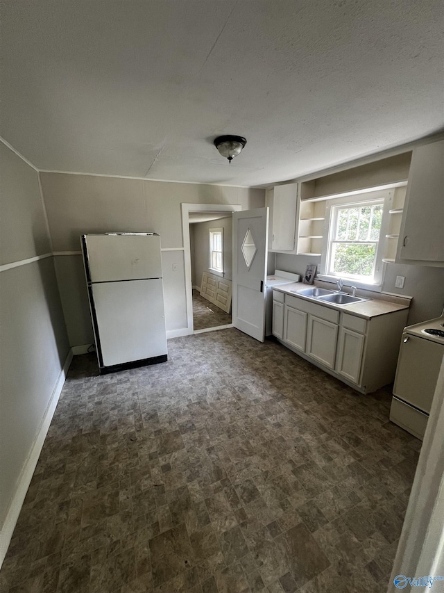 kitchen with freestanding refrigerator, open shelves, baseboards, stove, and a sink