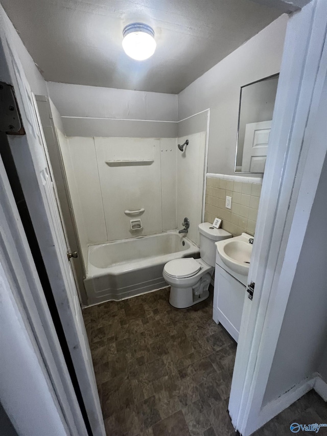 full bath featuring vanity, toilet, tile walls, washtub / shower combination, and stone finish floor