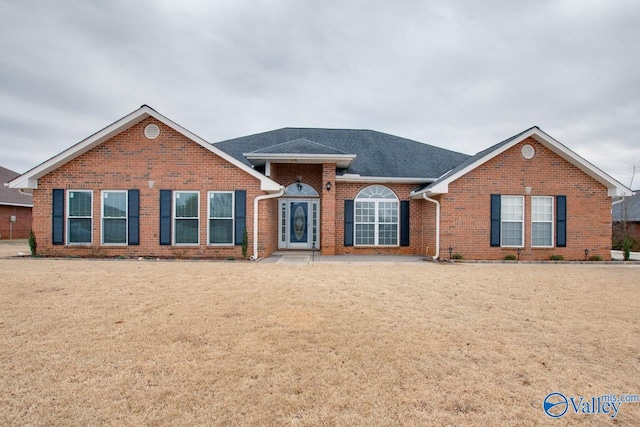 view of front of property featuring brick siding, a front lawn, and a shingled roof