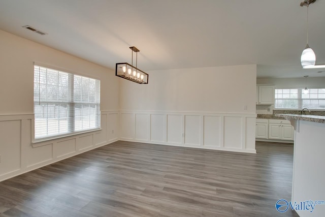 unfurnished dining area with a sink, visible vents, a decorative wall, and dark wood-style flooring