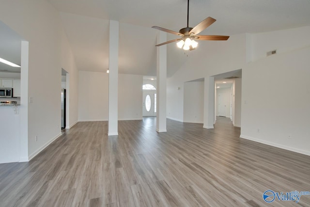 unfurnished living room with visible vents, light wood-style flooring, ceiling fan, high vaulted ceiling, and baseboards