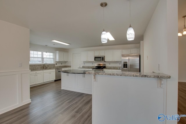 kitchen with stainless steel appliances, white cabinetry, a sink, and hanging light fixtures