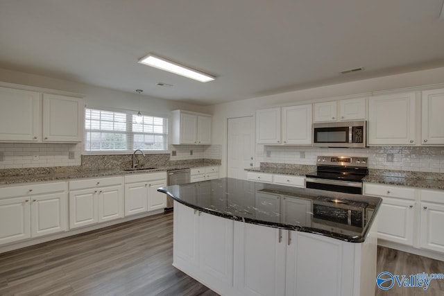 kitchen with appliances with stainless steel finishes, dark stone countertops, a kitchen island, and white cabinets