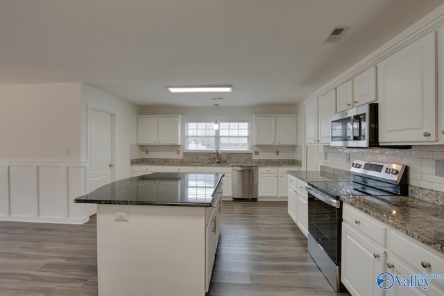 kitchen featuring stone counters, stainless steel appliances, visible vents, white cabinets, and a center island