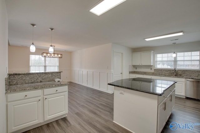 kitchen featuring a kitchen island, white cabinets, hanging light fixtures, stainless steel dishwasher, and dark stone countertops